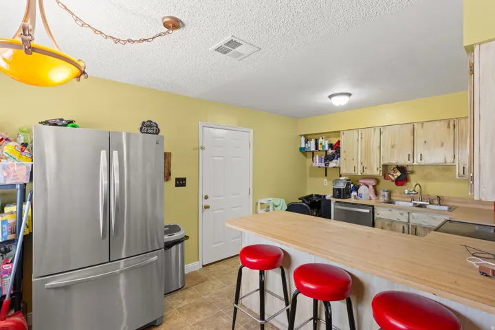 Kitchen featuring a breakfast bar, wood-finish countertops, natural wood cabinetry, a stainless steel dishwasher, and tile flooring