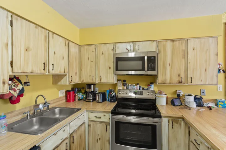 Kitchen featuring wood-finish cabinetry, stainless steel microwave, stainless steel range, double basin sink, and wood-finish countertops