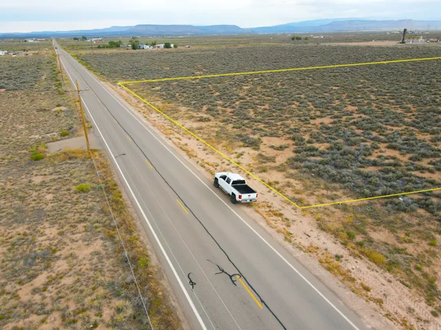 Expansive undeveloped lot featuring natural desert vegetation, a paved road frontage, and overhead utility lines