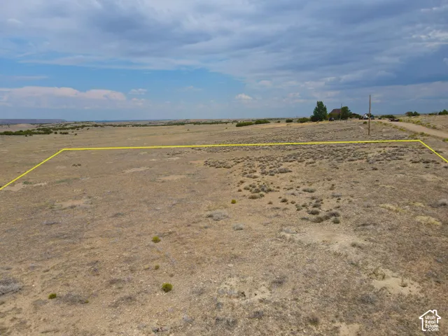 Expansive undeveloped land featuring natural desert vegetation, a gravel road, and distant structures