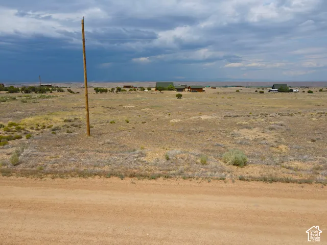 Expansive undeveloped land featuring a dirt road border, distant structures, and open sky