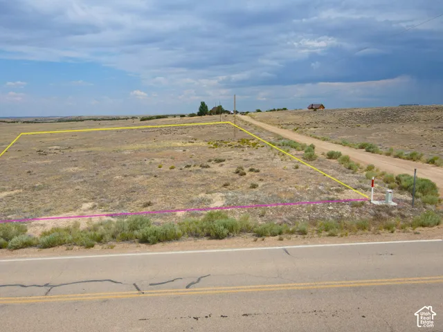 Expansive undeveloped land parcel featuring a paved road frontage, established dirt road access, and visible utility infrastructure, including a white utility box and red-capped post