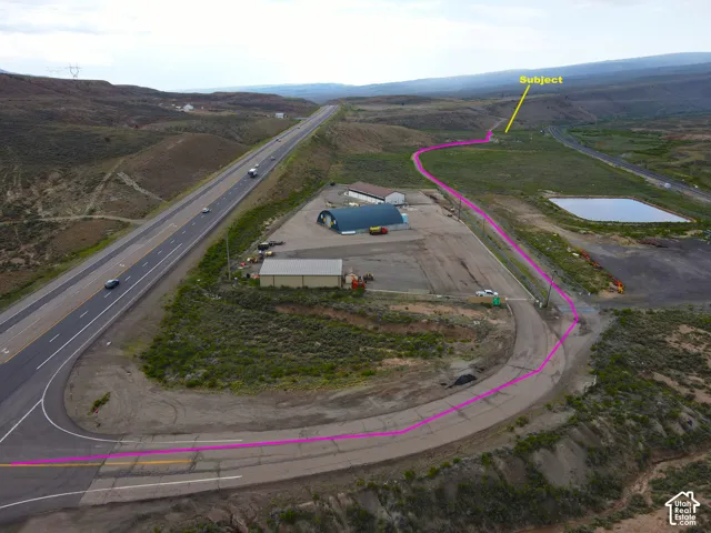 Expansive rural property featuring a paved highway frontage, secondary access road, multiple outbuildings, and a water retention pond