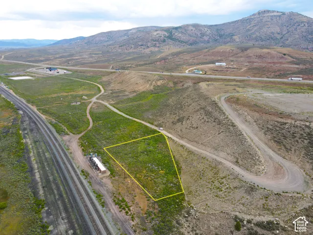 Expansive parcel of land bordered by a railway line and a winding dirt road, set against a backdrop of rolling hills and distant mountains