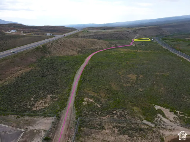 Expansive undeveloped land featuring a gravel access road, distant highway, and rolling hills