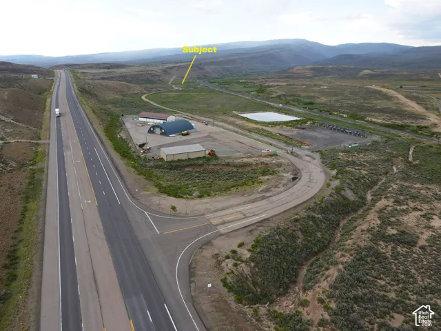 Expansive aerial overview showcasing a multi-lane highway, surrounding undeveloped land, and distant mountains