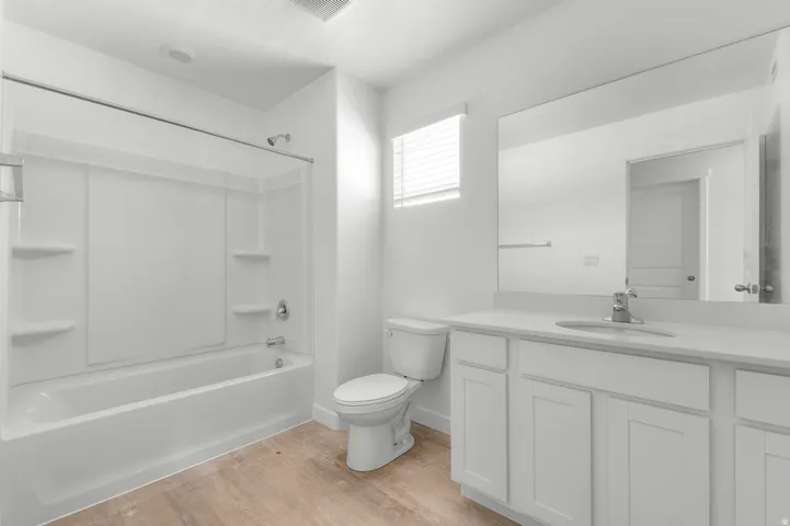 Modern bathroom featuring wood-finish flooring, a white vanity with a light-toned countertop, and a large wall-mounted mirror