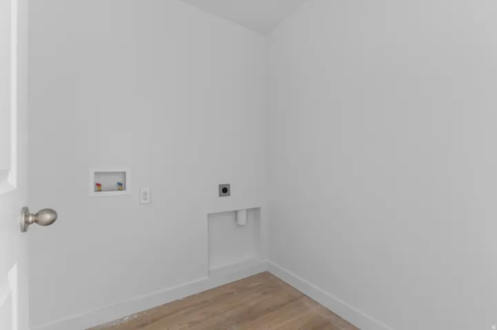 Dedicated laundry area featuring a door with a brushed nickel knob, white walls, and wood-finish flooring