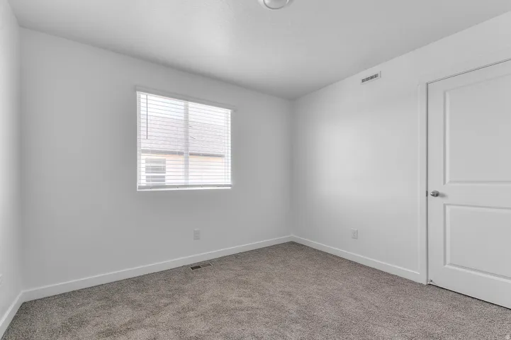 Bright room featuring a window with blinds, neutral-toned carpeting, white walls, white baseboards, and a white two-panel door with a brushed nickel knob