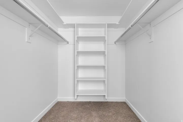 White closet system featuring a central shelving unit with five shelves, two clothing rods, and textured carpeting