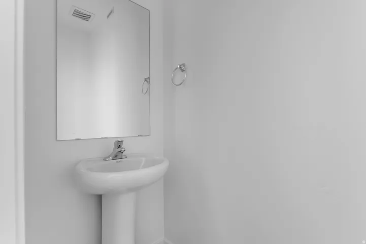Pedestal sink with chrome faucet, complemented by a frameless wall mirror and a towel ring