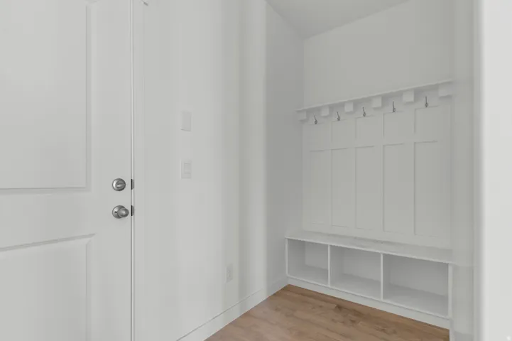 Entryway featuring built-in storage bench with open cubbies, wall-mounted coat hooks, and durable wood-finish flooring