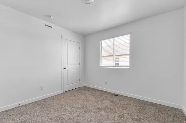 White-painted interior room featuring carpet flooring, a single window with horizontal blinds, and a white interior door with a silver-tone knob