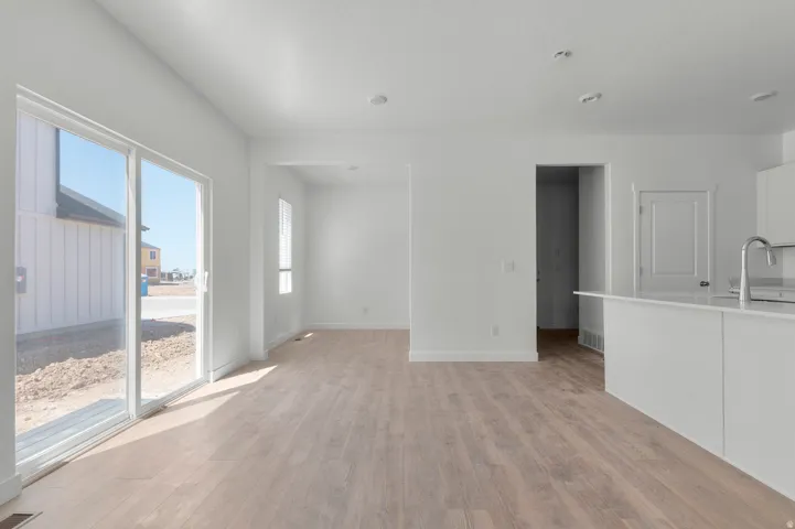 Open-concept living space with wood-finish flooring, white walls, recessed lighting, and a kitchen island with a stainless steel faucet