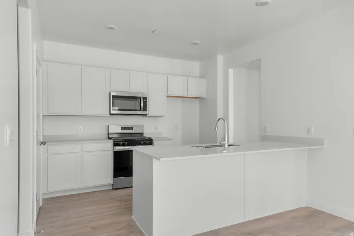 Bright kitchen featuring white shaker cabinetry, stainless steel microwave, gas range, light-toned countertops, and wood-finish flooring