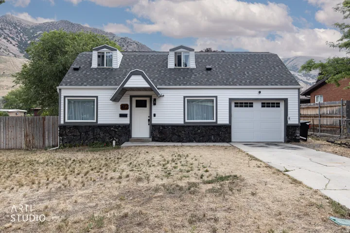 Classic white siding exterior with dark stone accents, featuring a prominent front door with an overhang, a single-car garage with divided light windows, and a dark shingle roof with three dormers