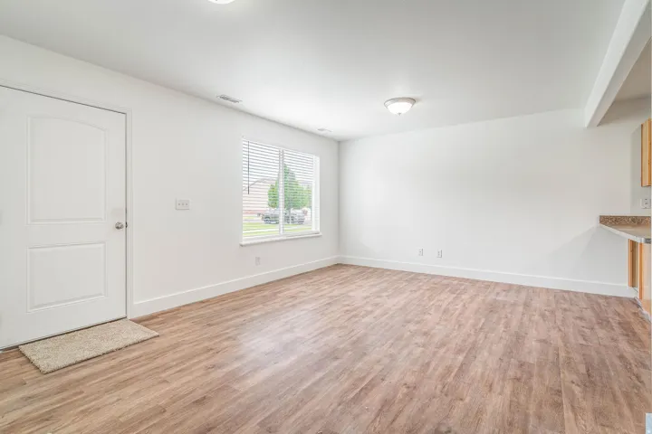 Spacious room featuring wood-finish flooring, white walls, and a large window with blinds