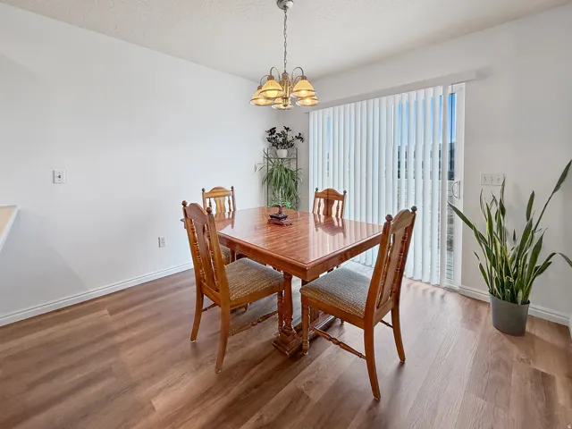 Dining area featuring wood-finish flooring, a contemporary chandelier, and a sliding glass door with vertical blinds