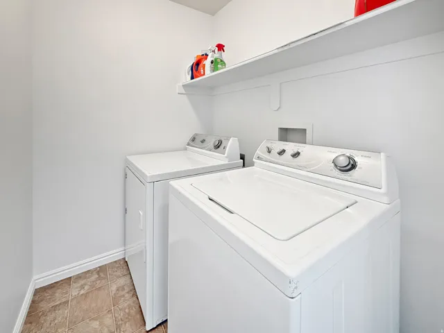 Dedicated laundry area featuring a white built-in shelf, white walls, and stone-finish tile flooring