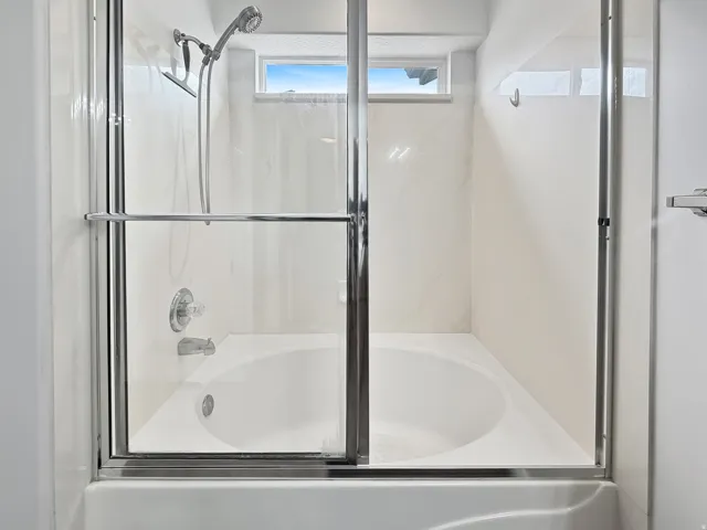 Tub and shower combination featuring a large garden tub, clear glass sliding doors with chrome framing, white tiled walls, a chrome showerhead with handheld sprayer, and a chrome tub spout