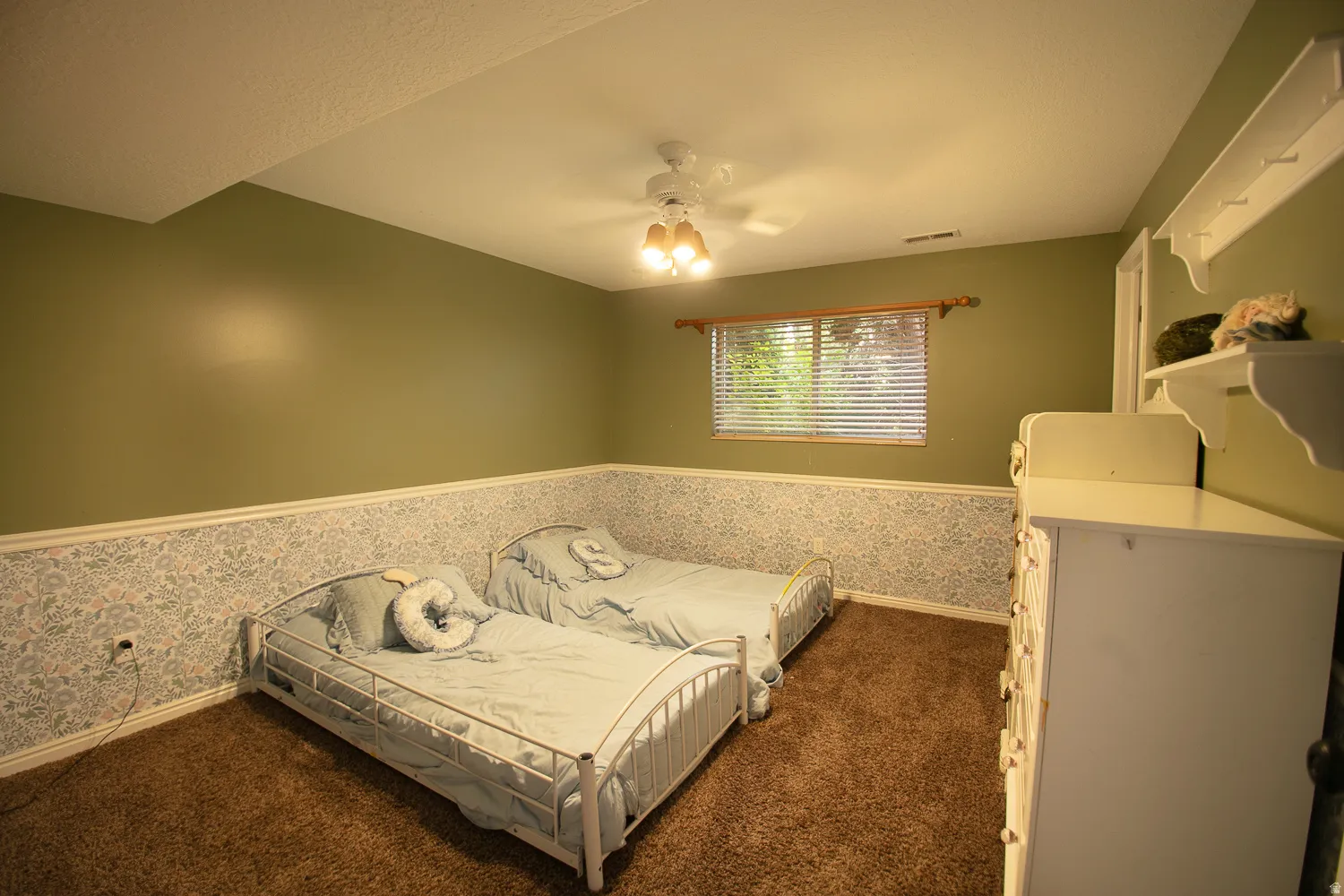 Carpeted room with a ceiling fan light fixture, a window featuring blinds, and walls with a patterned wainscoting