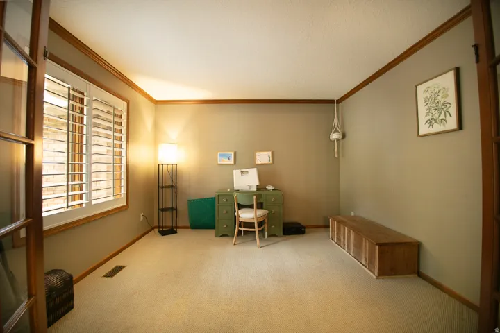 French doors opening to a room with plantation shutters, wood trim, and light-colored carpeting