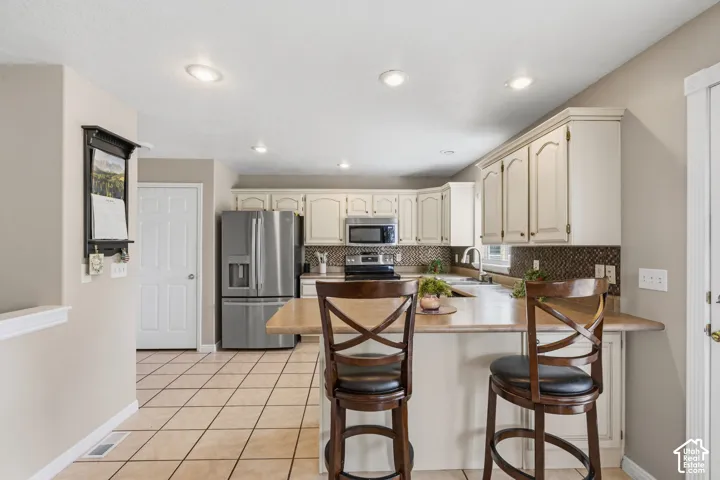 Kitchen featuring light-toned cabinetry, stainless steel appliances, a breakfast bar, recessed lighting, and tile flooring