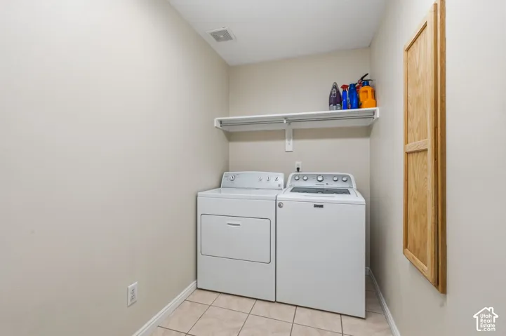 Dedicated laundry area featuring a white washer and dryer, tiled flooring, an overhead storage shelf, and a built-in wooden cabinet