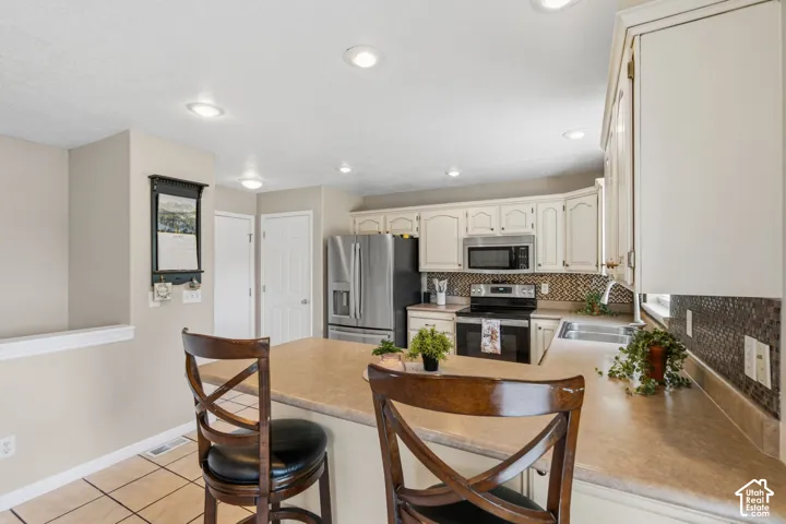 Kitchen featuring a peninsula counter with seating, white cabinetry, integrated stainless-steel appliances, a tiled backsplash, and recessed lighting