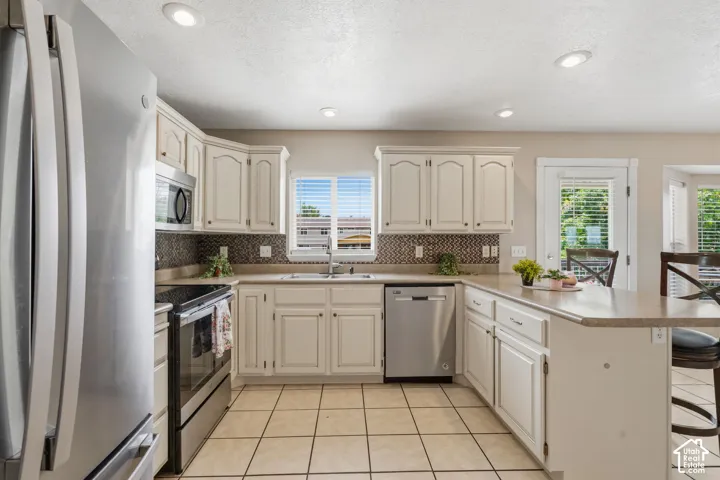 Kitchen featuring white cabinetry, stainless steel appliances, a patterned tile backsplash, and a light-toned countertop