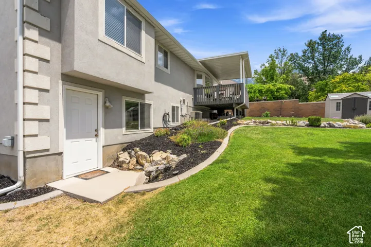 Expansive green lawn with a curved landscape bed, a covered upper-level deck, and a detached storage shed