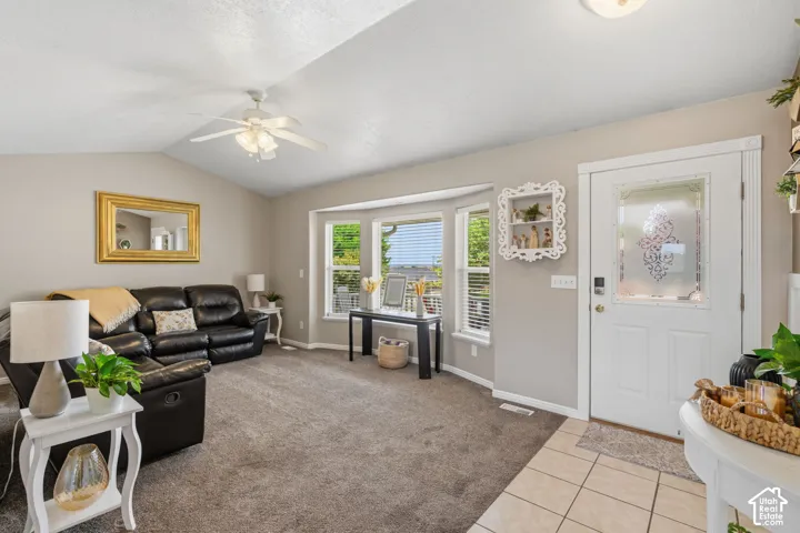 Spacious living area featuring vaulted ceilings with a ceiling fan, carpet flooring, and a bay window