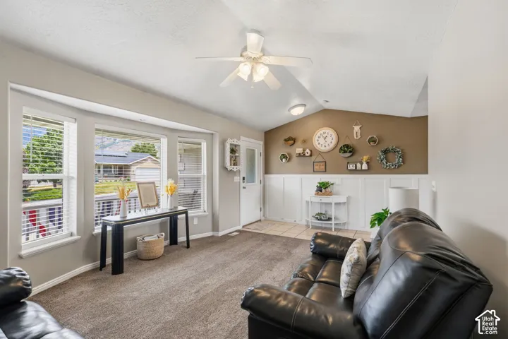Living area featuring a vaulted ceiling with a ceiling fan, a bay window with multiple panes, and wall paneling