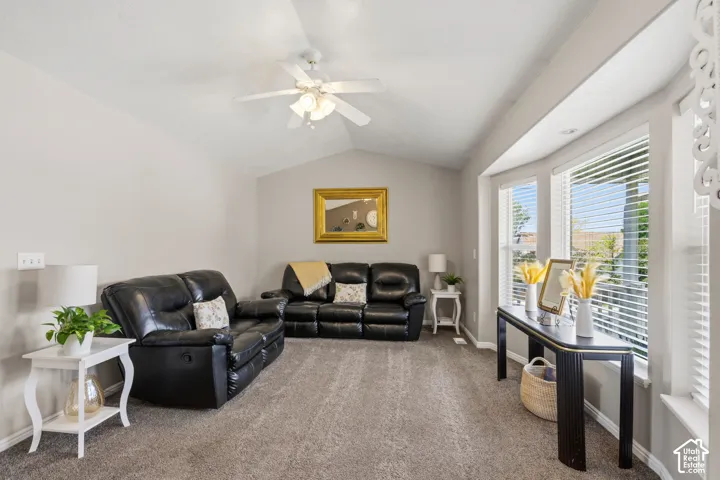 Living area featuring vaulted ceilings, a ceiling fan, bay windows with blinds, and neutral-toned carpeting
