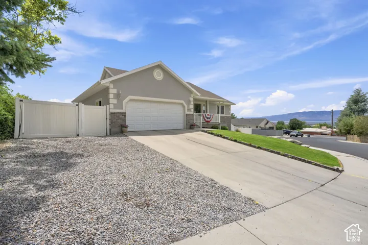 Ranch-style residence featuring a two-car garage, covered front porch, gravel parking area, and a private side-yard gate