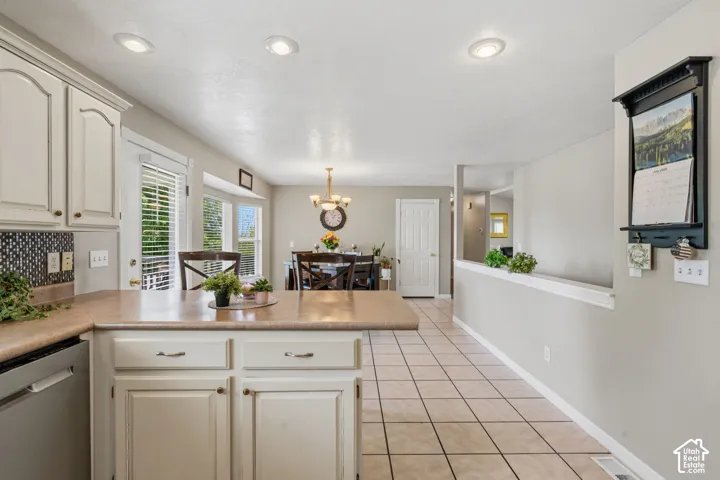 Open-concept kitchen featuring cream cabinetry, a stone-look countertop, tile backsplash, and stainless steel dishwasher