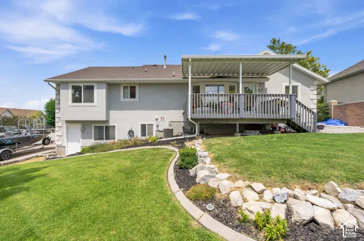 Rear exterior featuring a covered deck, stucco siding, a lower-level entry door, and a sloping lawn with decorative rock landscaping