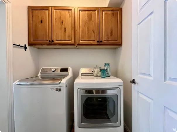 Laundry area featuring two appliances, overhead wood cabinetry with black hardware, a wall-mounted drying rack, and white paneled door