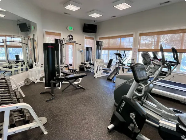 Fitness center featuring rubberized flooring, abundant natural light from multiple windows, recessed lighting, wall-mounted mirrors, and built-in weight racks