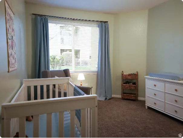 Carpeted interior room featuring a large window with blinds and drapes, light-toned walls, and white baseboards
