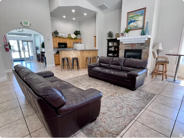 Spacious common area featuring vaulted ceilings, a built-in fireplace with a stone surround, and an integrated wet bar with wood-finish cabinetry