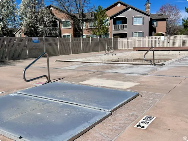 Community pool area featuring a perimeter fence, surrounding buildings, and a clear sky