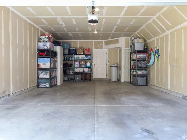 Spacious garage featuring a concrete floor, exposed drywall walls, a garage door opener, and a service door