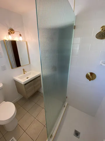 Bathroom featuring a fluted glass shower partition, white subway tile shower surround, and brushed gold fixtures