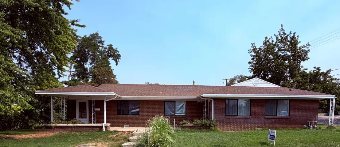 Brick-clad exterior featuring a front porch with white columns, a brown shingle roof, white gutters, and multiple windows