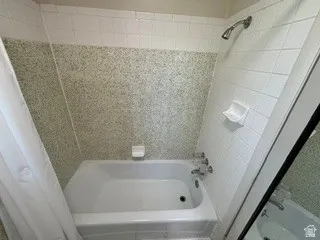 Bathtub and shower combination featuring white subway tile, speckled green wall tile, chrome shower head, and chrome tub fixtures