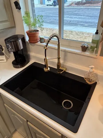 Deep black composite sink with integrated drying rack, featuring a gold-finish spring-neck pull-down faucet