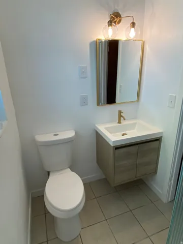 Modern bathroom featuring a floating wood-finish vanity with an integrated sink, a gold-framed mirror, and a contemporary brass-finish light fixture