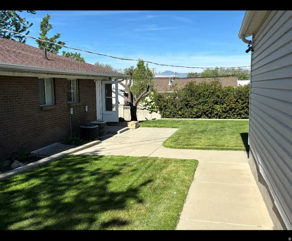 Expansive outdoor area featuring a brick exterior, a concrete patio, a manicured lawn, and mature landscaping