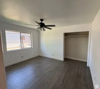 Bright interior space featuring wood-finish flooring, a ceiling fan with integrated lighting, a spacious window, and an open closet with a built-in hanging rod